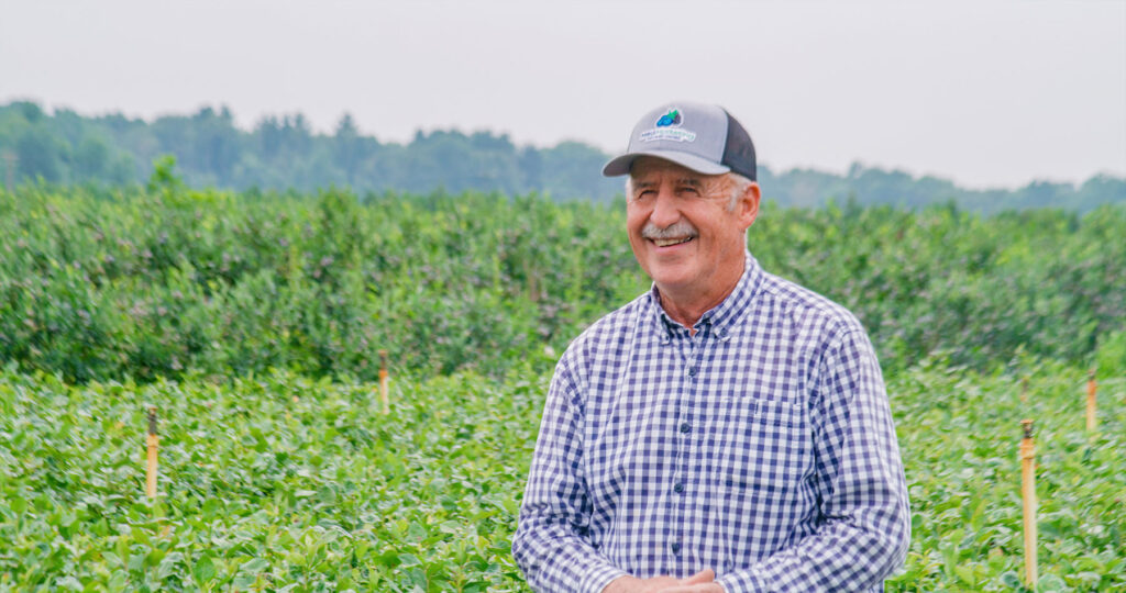 blueberry grower in field smiling wearing a baseball cap