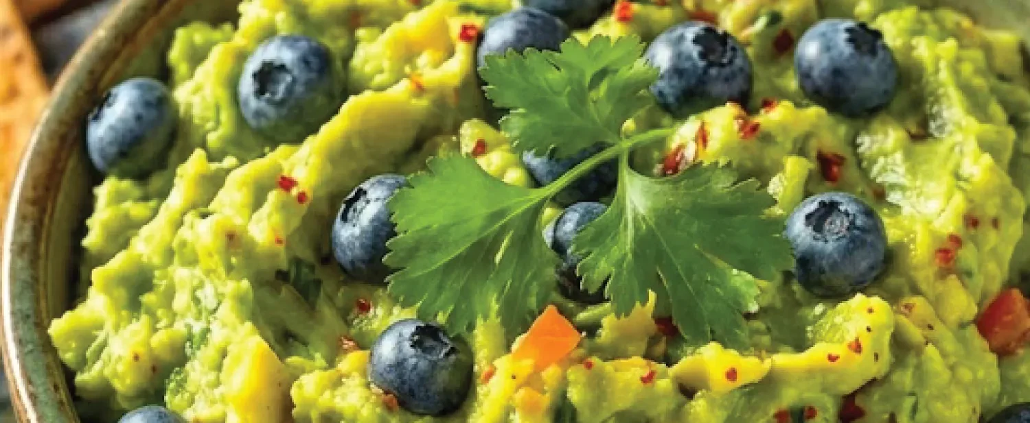 Blueberry-Lime Jalapeño Guacamole in bowl with cut avocados in background
