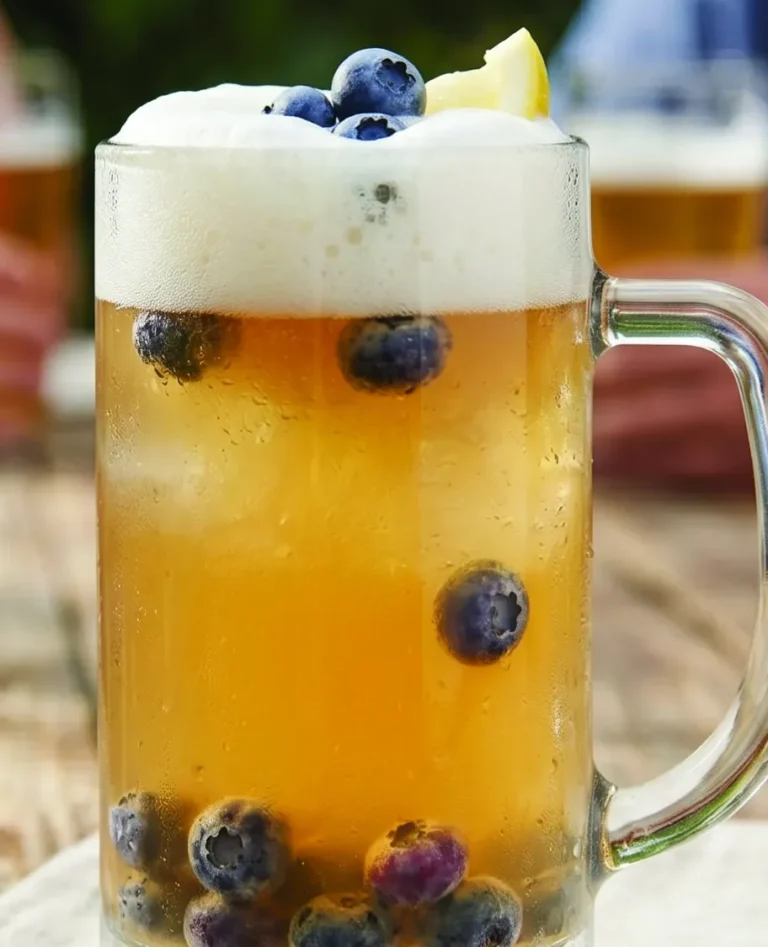 frosted mug of blueberry shandy drink with foamy top and blueberries floating inside